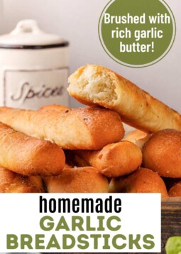 Homemade garlic breadsticks in a bread basket. Text overlay reads brushed with rich garlic butter.