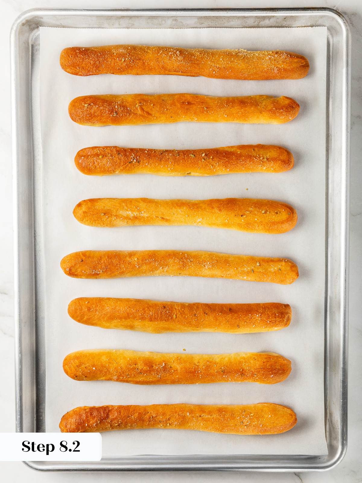 Freshly baked garlic breadsticks cooling on baking sheet with golden tops.