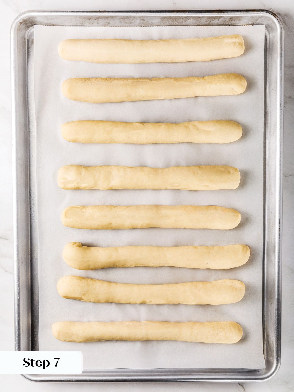 Shaped breadstick dough resting on baking sheet during second rise.
