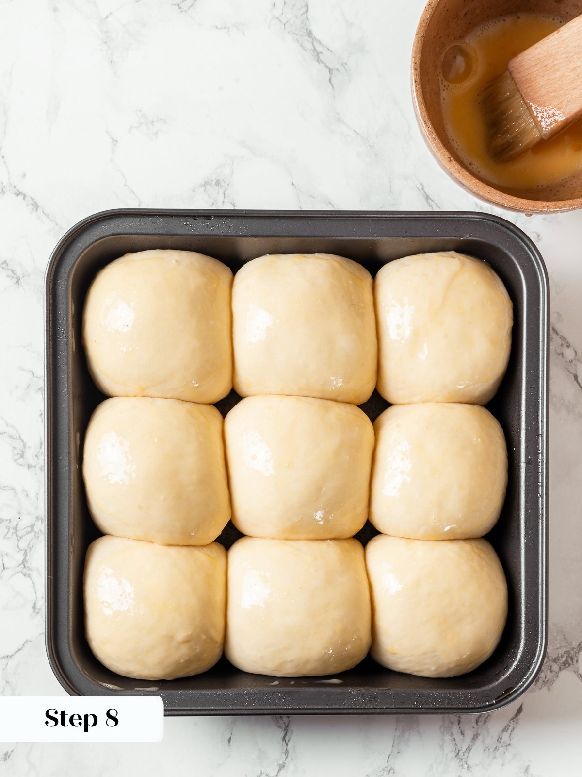 Egg wash brushed over milk bread rolls before baking for golden crust.