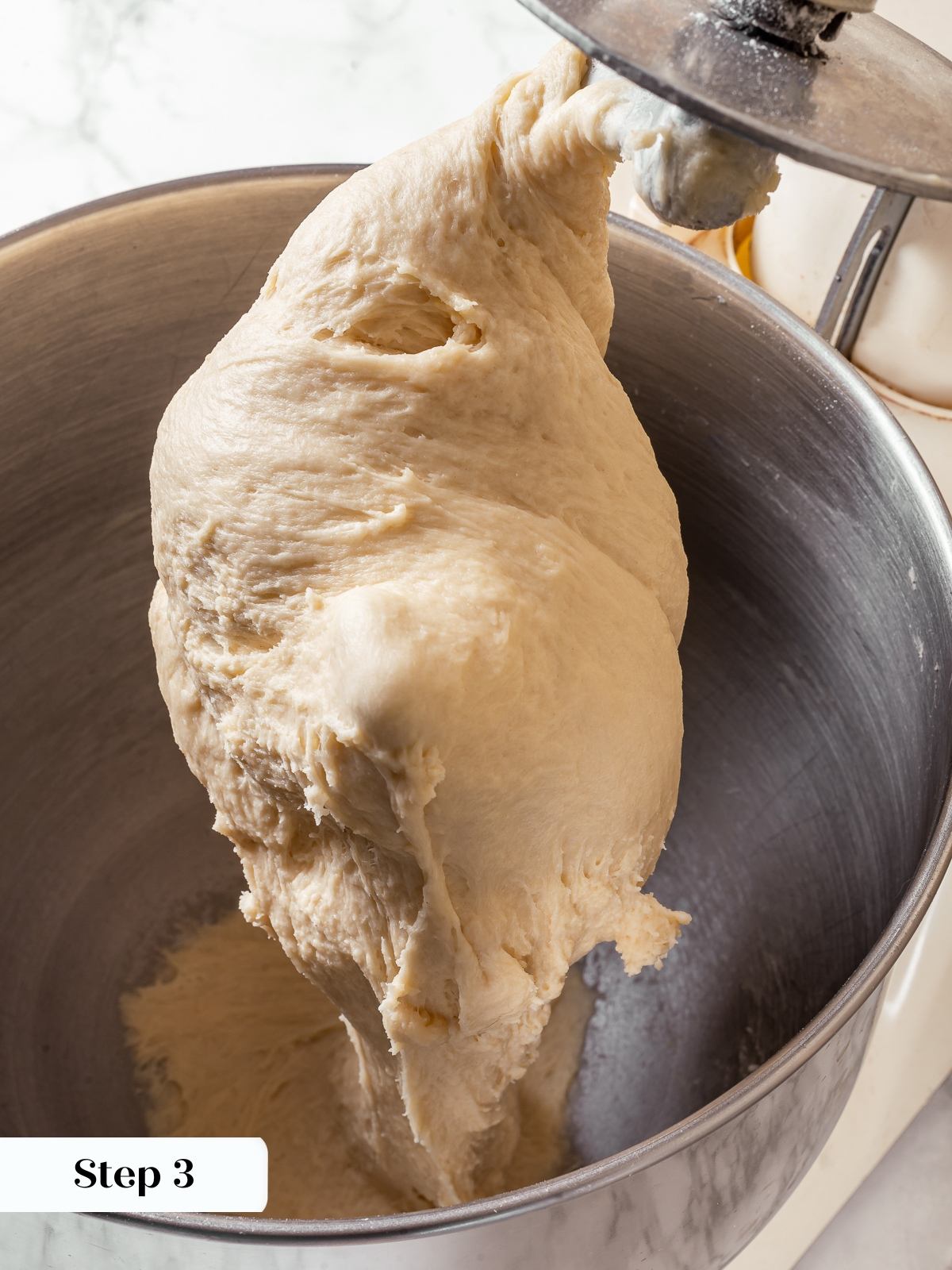 Milk bread dough mixing in stand mixer bowl with dough hook attachment.