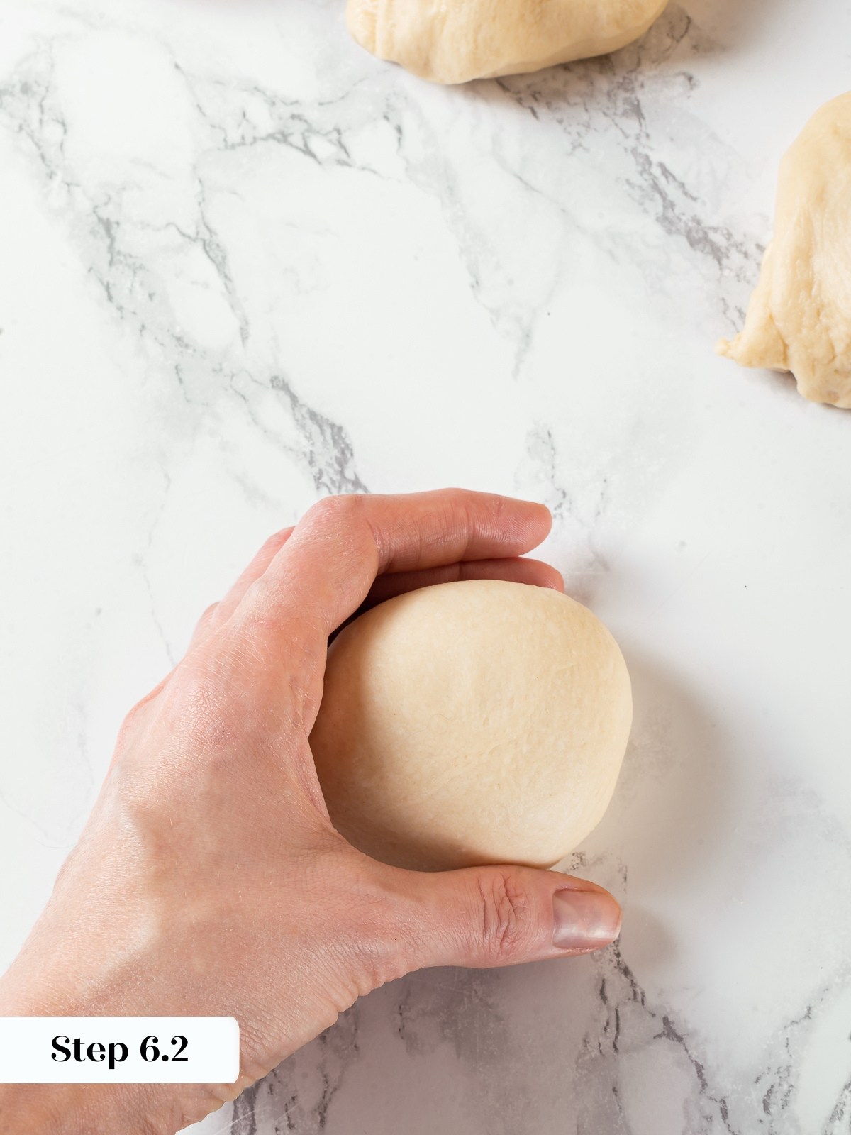 Hands rolling dough into smooth balls for milk bread rolls.