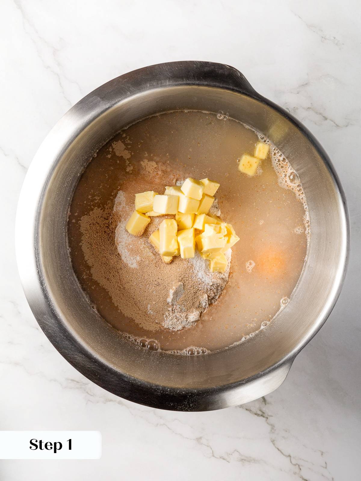 Stand mixer bowl combining whole wheat flour yeast water butter egg and sugar.