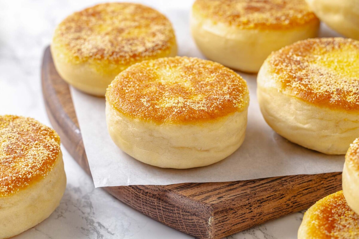 Fully baked English muffins with golden crust and firm exterior resting after cooking.