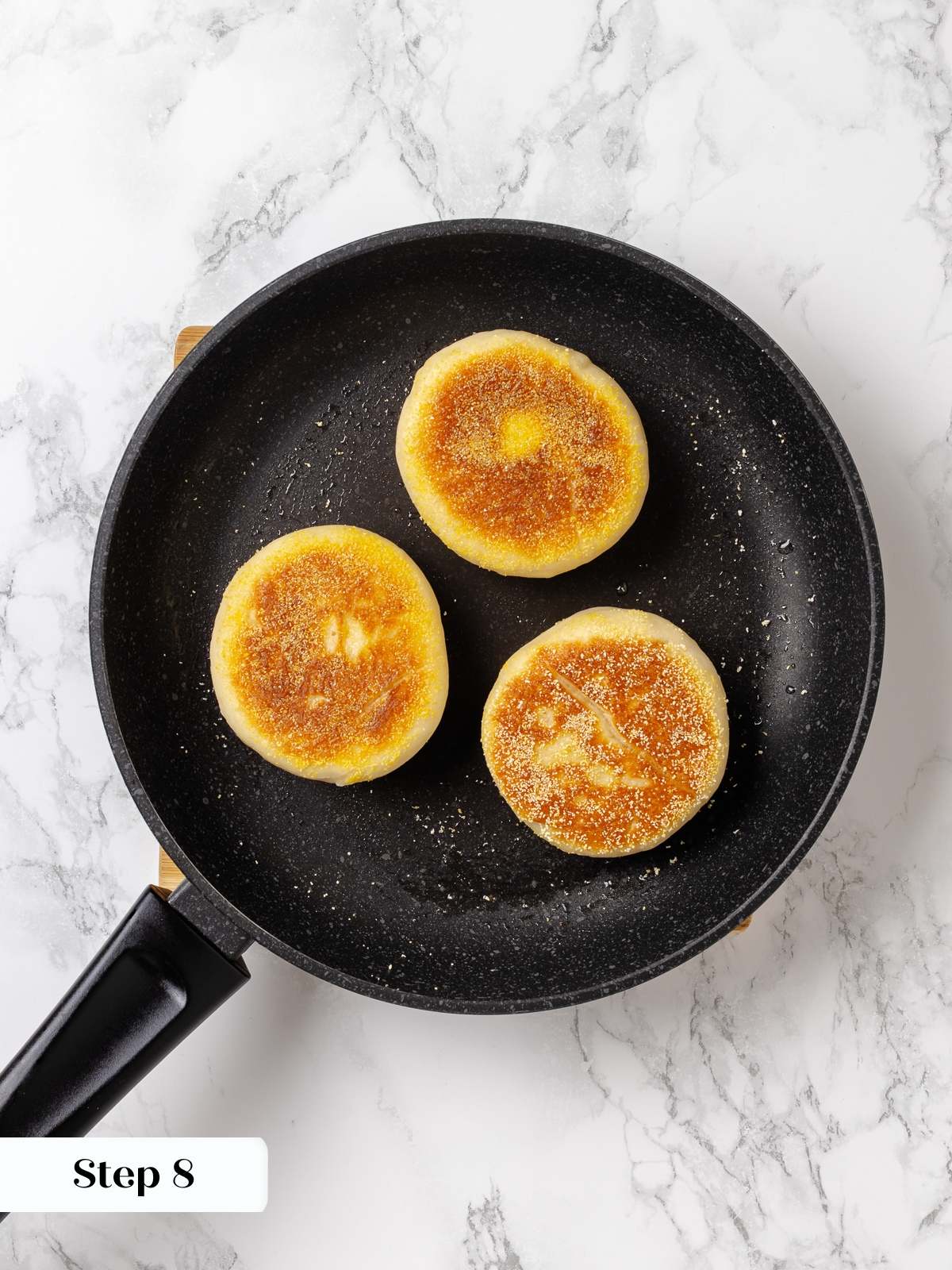 English muffins cooking in skillet with butter and oil developing golden crust on each side.