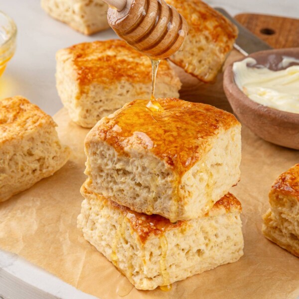 Sourdough biscuits drizzled with honey, emphasizing glossy finish and warm, tender crumb.