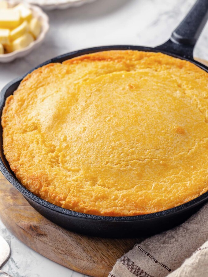 Sourdough cornbread resting in cast iron skillet with browned butter edges and rustic texture.