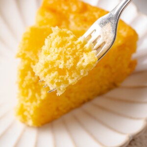 Fork lifting a bite of sourdough cornbread showing moist crumb and soft, tender texture.