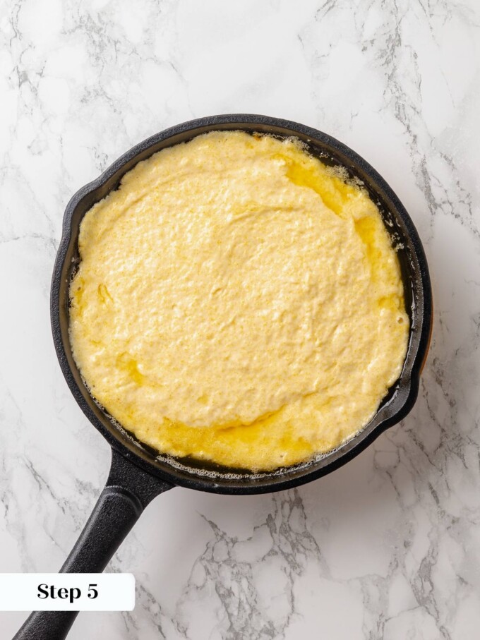 Thick batter spread in preheated skillet ready for baking with butter sizzling underneath.