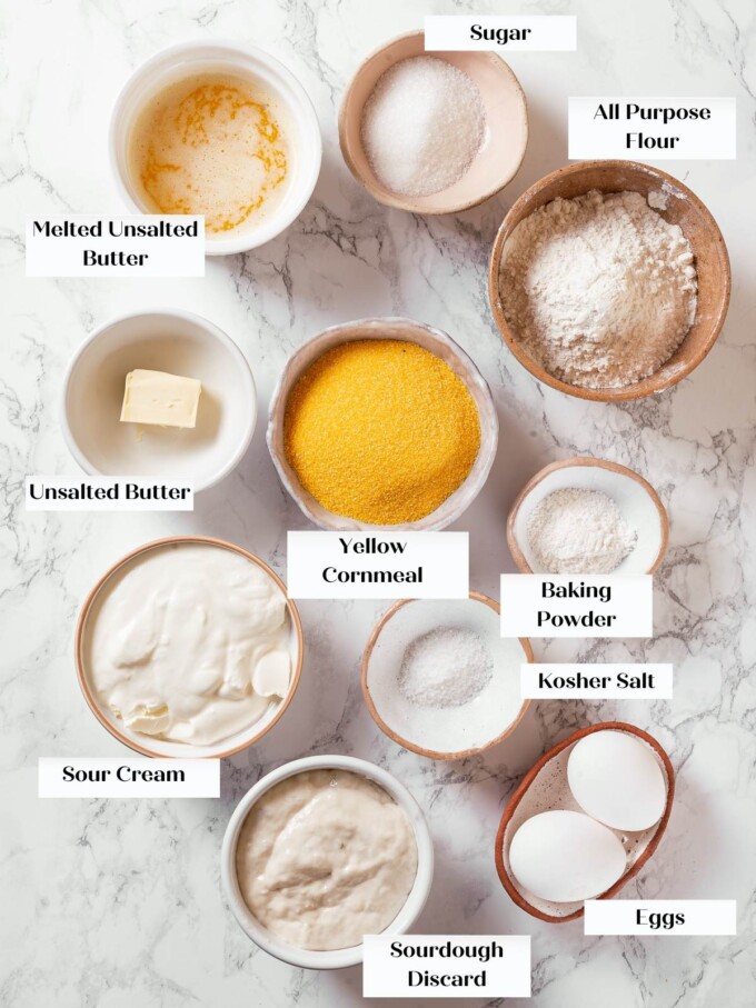 Measured ingredients for sourdough cornbread arranged including cornmeal, flour, eggs, and butter.