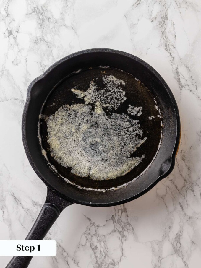 Cast iron skillet heating with butter melting and beginning to brown for crispy edges.