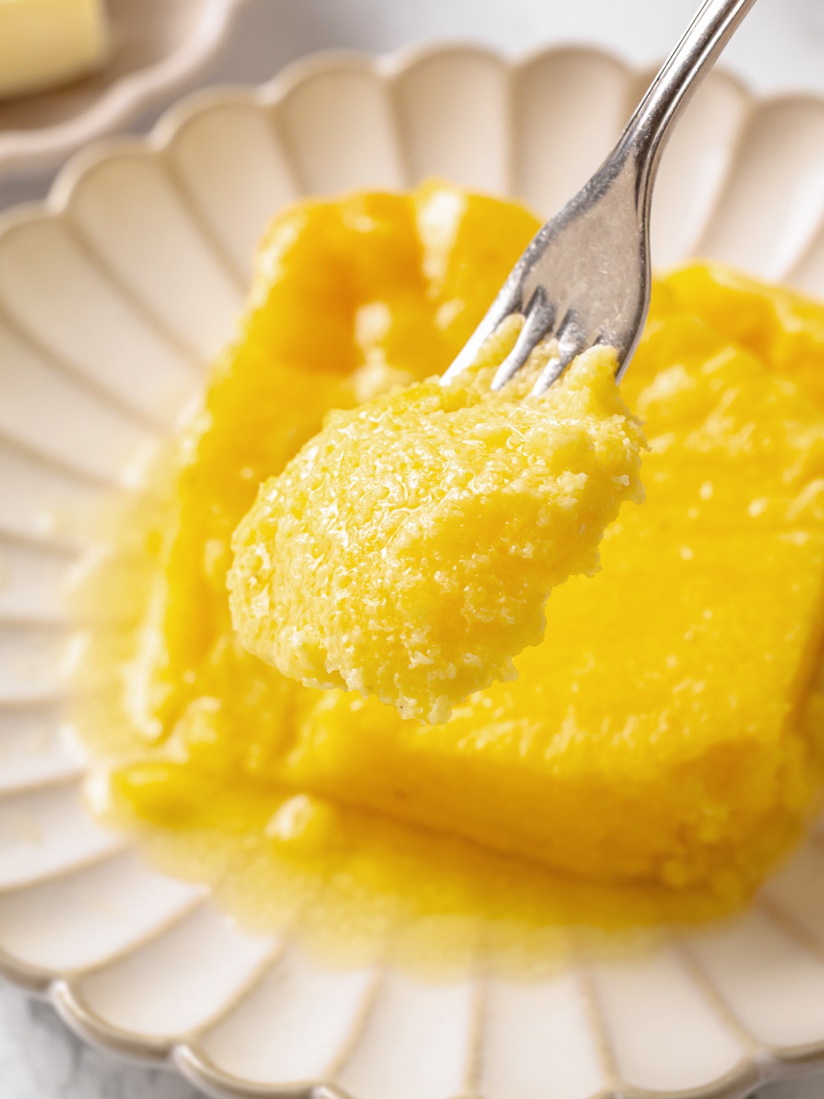 Fork lifting soft spoon bread showing airy interior and custardy texture with tender crumb.