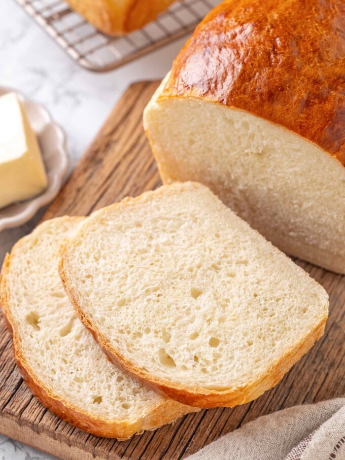 Cut buttermilk loaf on wooden board showing pillowy white crumb beside two thick slices.