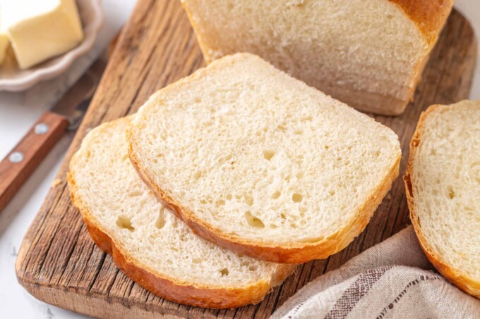 Buttermilk bread slices fanned on rustic board with butter dish and bread knife nearby.