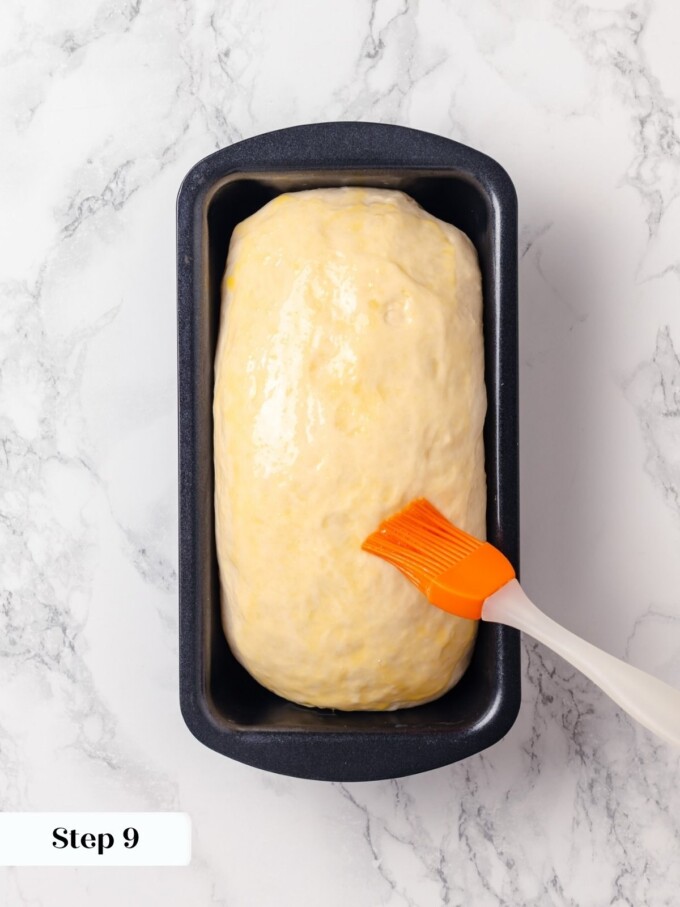 Orange silicone brush applying beaten egg wash onto risen buttermilk dough in pan.