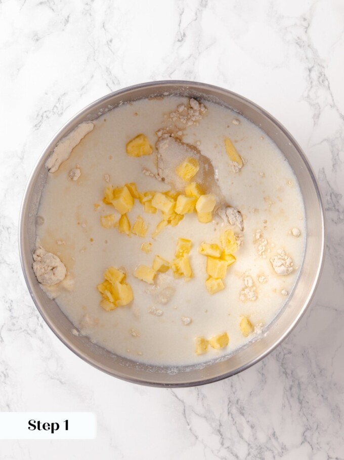 Buttermilk, butter cubes, and dry ingredients combined in stand mixer bowl ready to mix.
