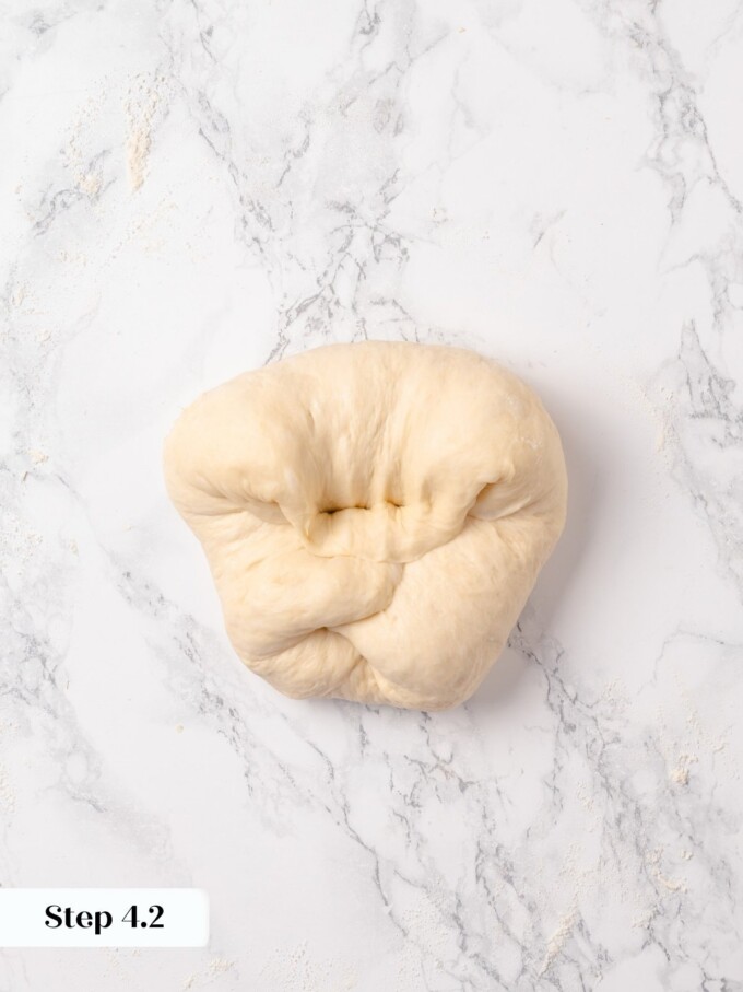 Folded buttermilk dough with pinched seam visible after preshape fold on marble.