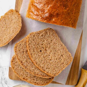 Whole wheat sandwich loaf with three thick slices arranged on wooden board with butter.