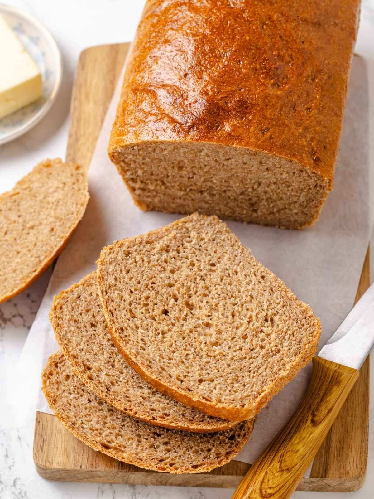 Three slices fanned out from a tall whole wheat sandwich loaf with butter.