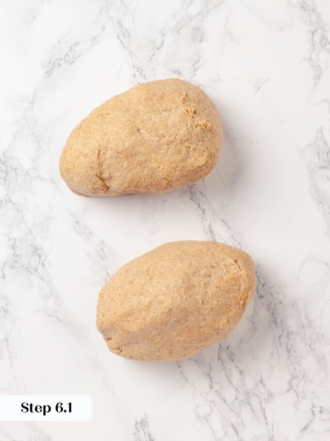 Two equal pieces of whole wheat bread dough divided and resting on marble.