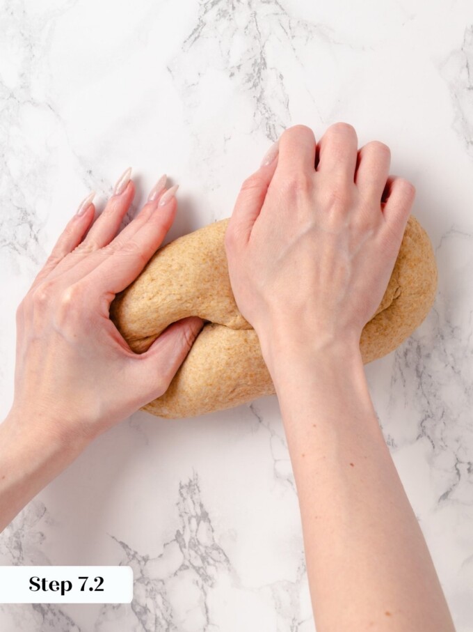 Hands shaping bread dough into a sandwich loaf with seam pinched underneath.