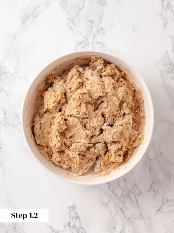 Shaggy whole wheat dough mid mix inside a wide white ceramic bowl on marble.