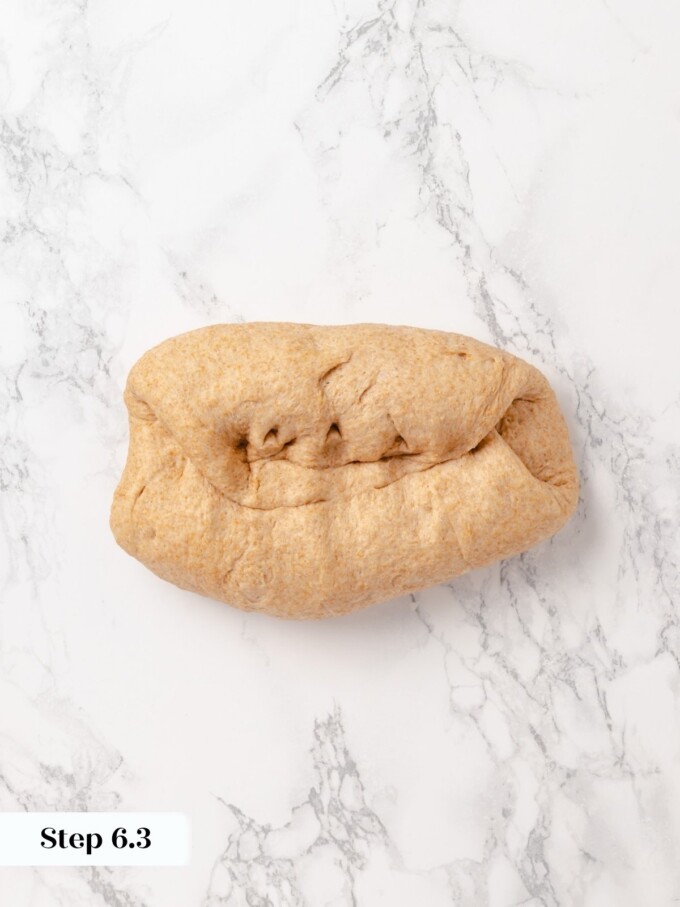 Folded whole wheat bread dough resting on white marble counter after second pre-shape fold.
