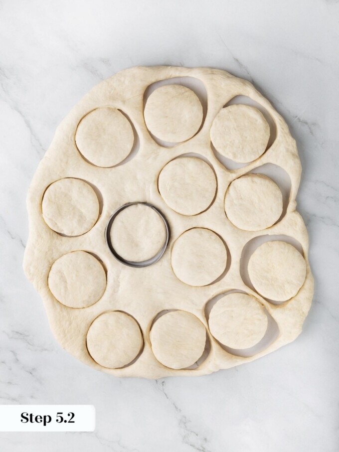Pressed sourdough dough with cut rounds and a metal biscuit cutter on a marble work surface.