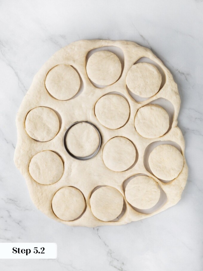 Pressed sourdough dough with cut rounds and a metal biscuit cutter on a marble work surface.