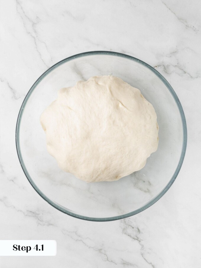 Sourdough English muffin dough degassed and folded down in a glass bowl after the first proof.