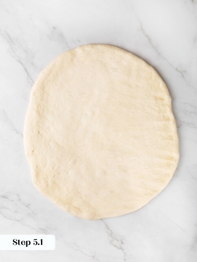Sourdough dough pressed into a flat circle about a quarter inch thick on a marble surface.