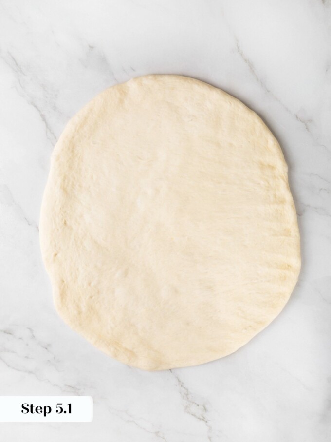 Sourdough dough pressed into a flat circle about a quarter inch thick on a marble surface.