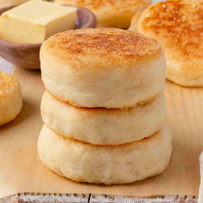 Three sourdough English muffins stacked on parchment paper with a butter dish in the background.