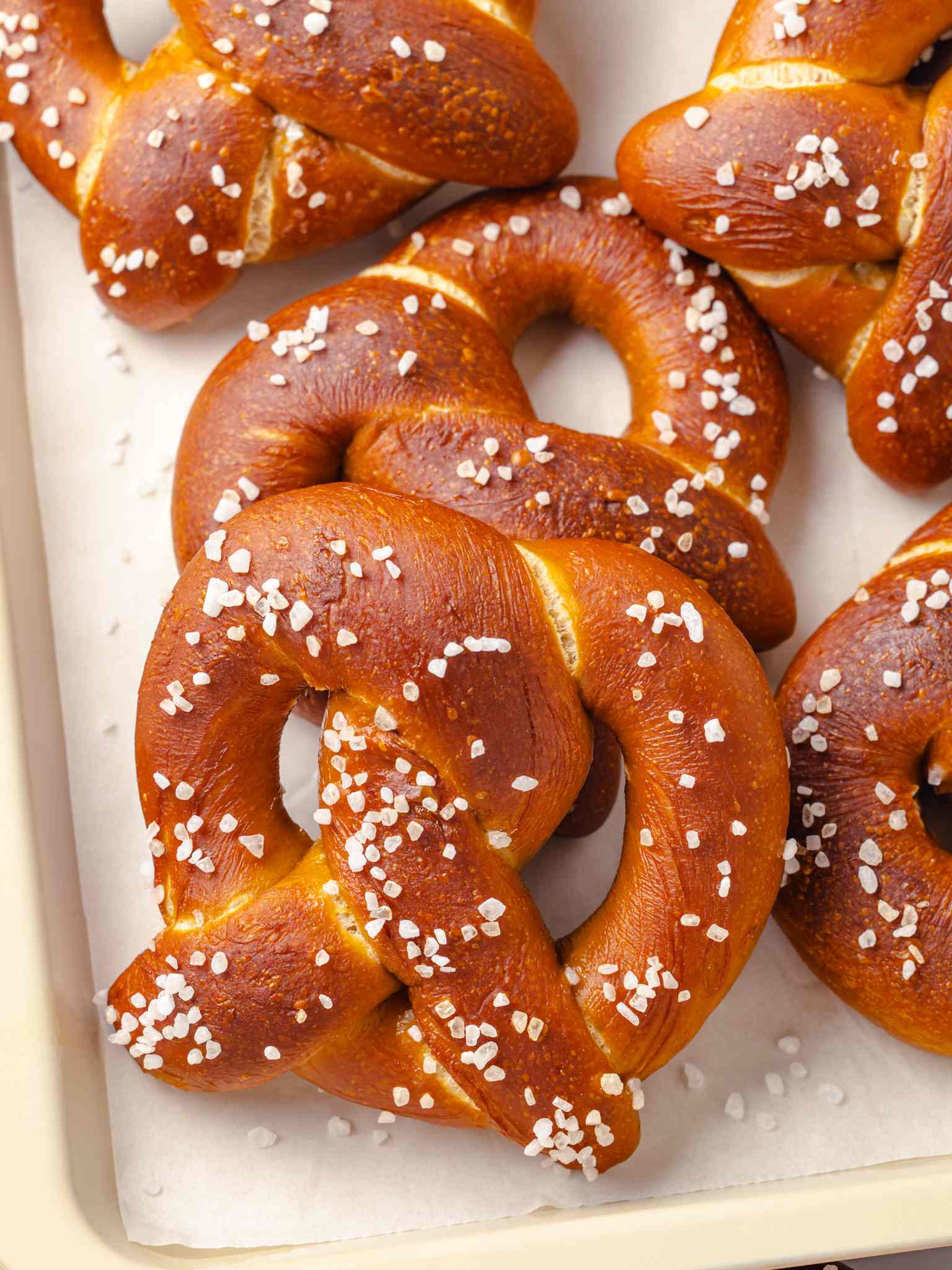 Several golden-brown pretzels clustered together on a wooden cutting board with white parchment paper underneath.