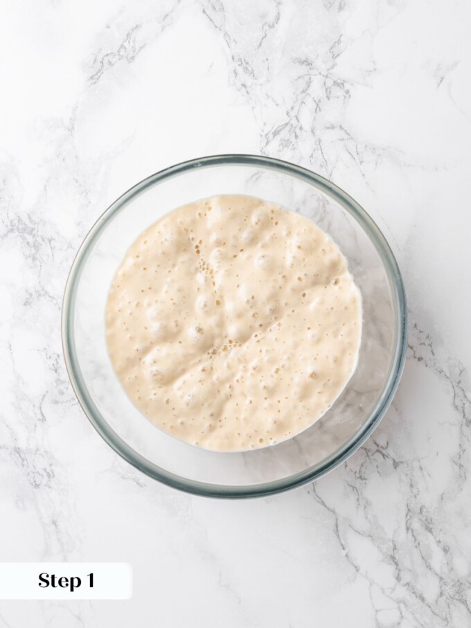 Bubbly active sourdough build domed across the surface of a clear glass mixing bowl.