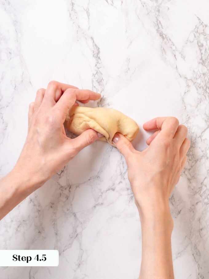 Hands sealing the seam of a small preshaped pretzel dough piece on a marble countertop.