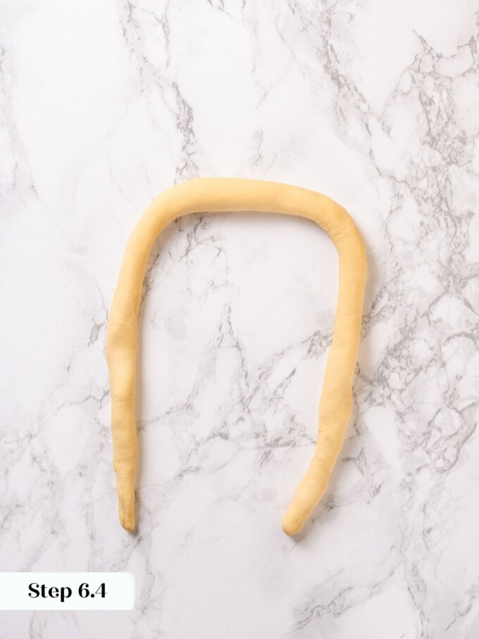 A long pretzel rope curved into a wide U shape on a white marble work surface.