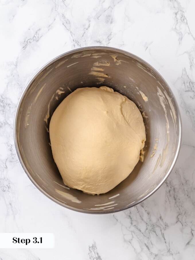 Smooth pretzel dough gathered into a cohesive ball inside a stainless steel mixer bowl after kneading.