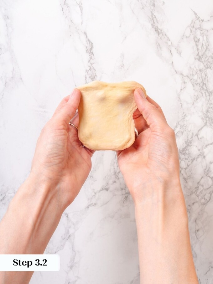 Hands stretching a small piece of pale dough thin between fingers to test gluten development.