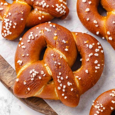 Single salted pretzel with glossy dark crust framed by surrounding pretzels in a tight square arrangement.