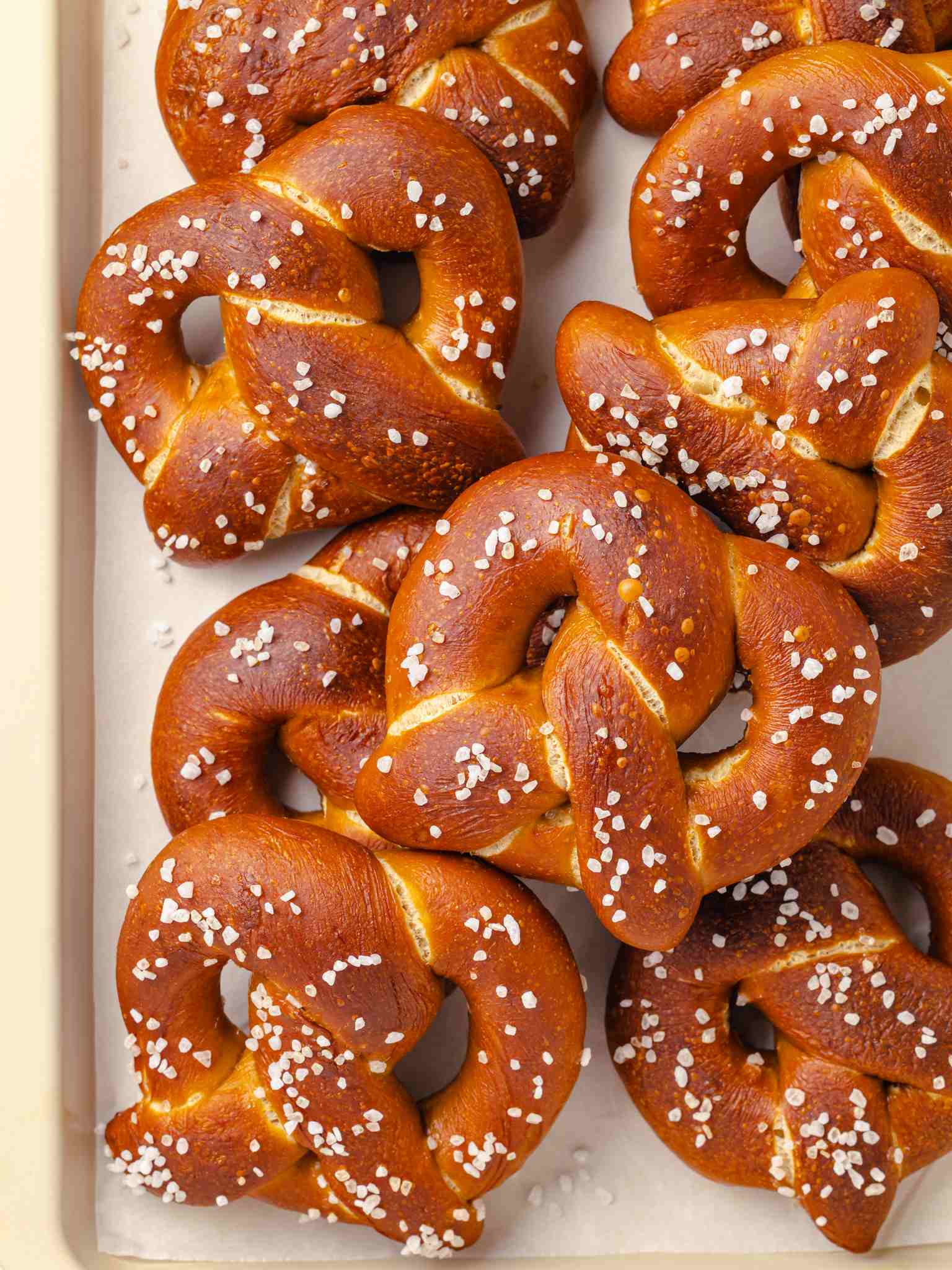 Several glossy mahogany pretzels piled together with coarse white salt scattered across their tops.