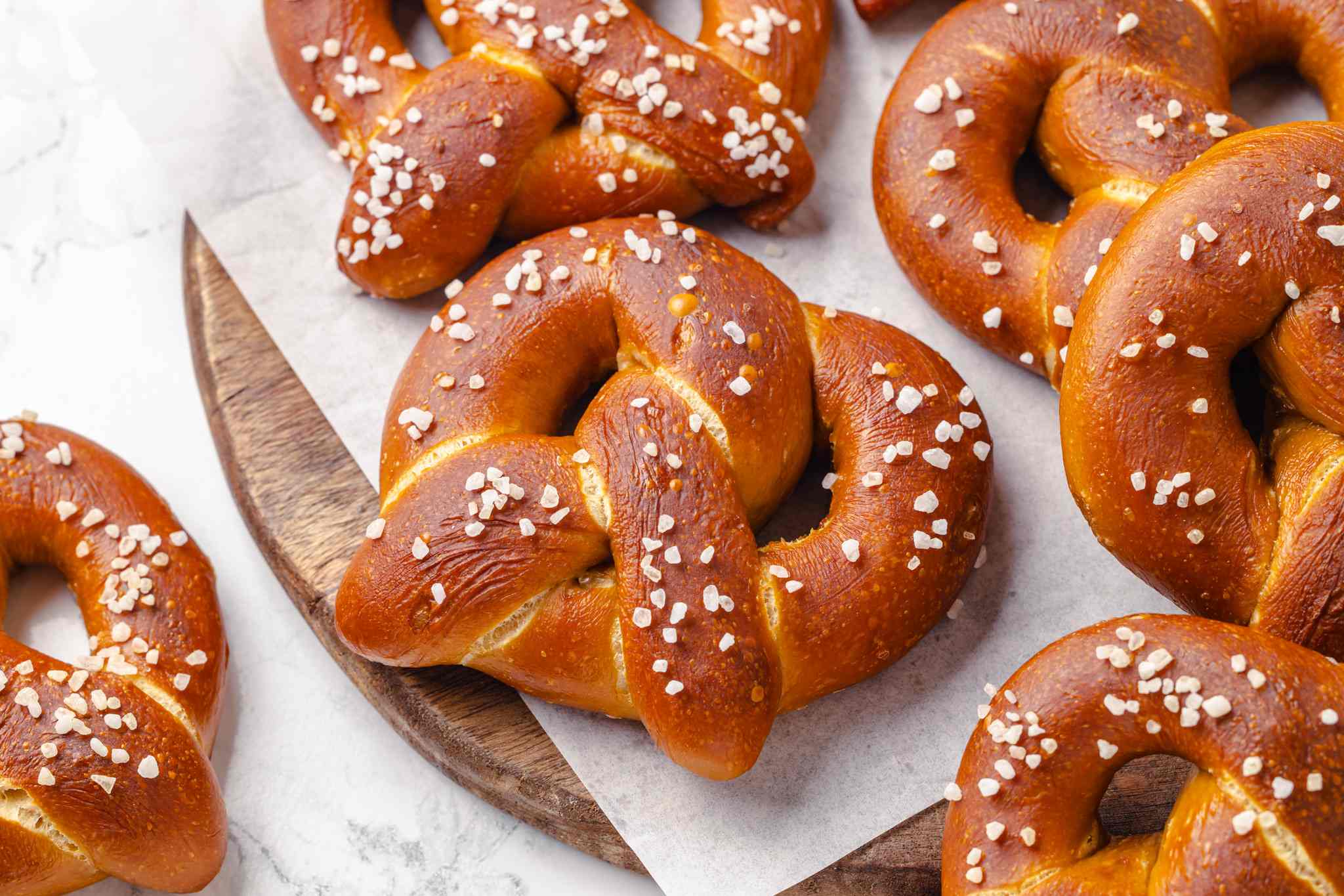 Several golden-brown pretzels clustered together on a wooden cutting board with white parchment paper underneath.
