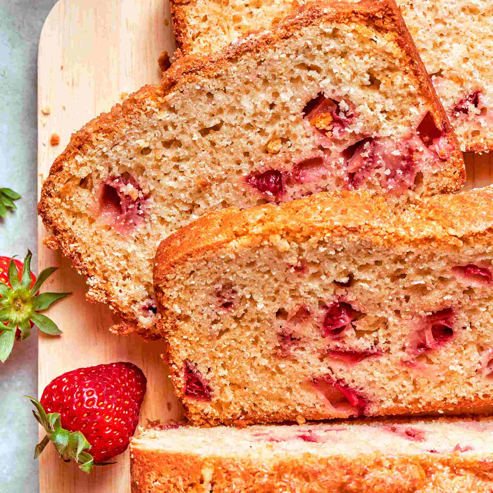 Square crop of strawberry bread slices revealing tender crumb and bright pink berry pieces.