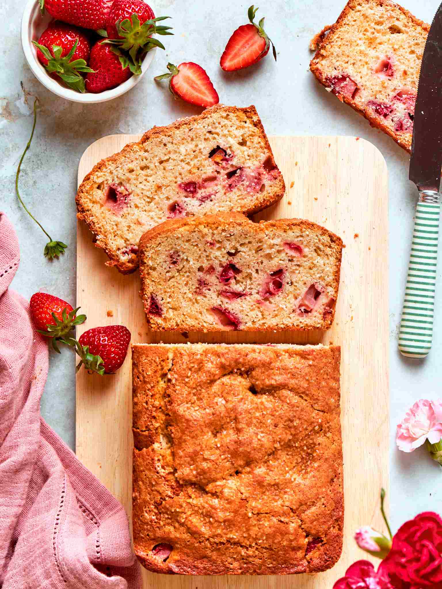 Strawberry bread sliced on a wooden board with two slices fanned on top showing tender pink crumb.