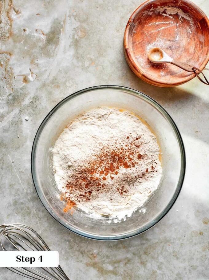 Dry ingredients sprinkled with cinnamon resting on the surface of wet batter, ready to be folded together.