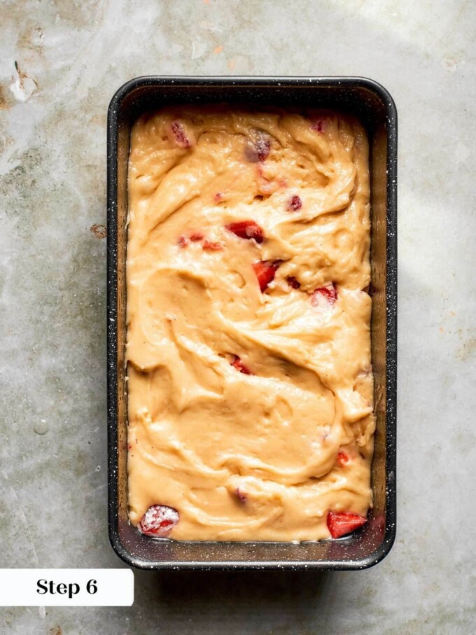 Strawberry bread batter spread evenly in a dark loaf pan, with chunks of berries visible throughout.