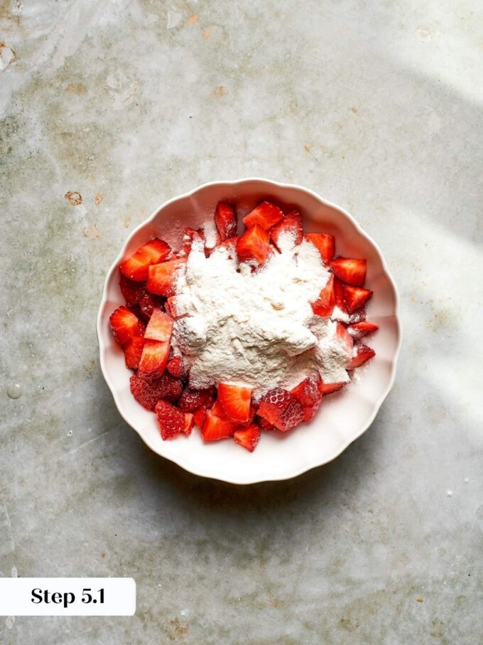 Chopped strawberries surrounded by all-purpose flour in a small ceramic bowl before being coated.