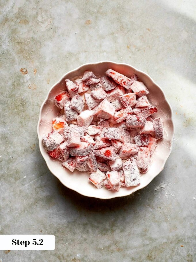 Diced strawberries fully coated in flour, sitting in a fluted ceramic bowl on a stone surface.