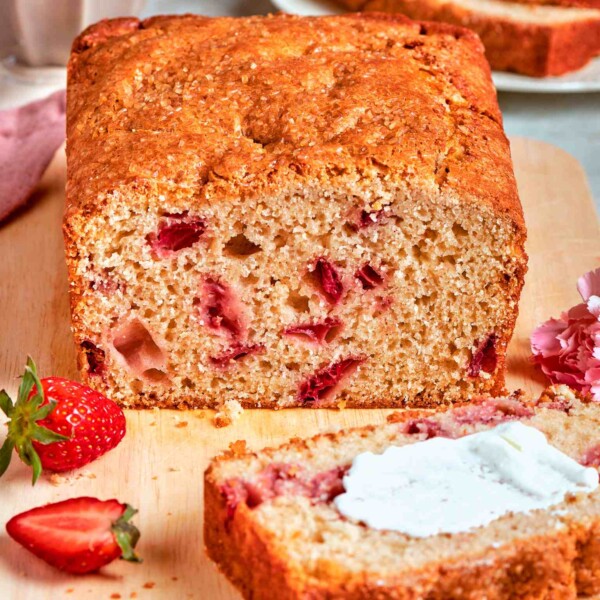 Strawberry bread loaf with a slice spread thickly with cream beside fresh strawberries and pink carnations.