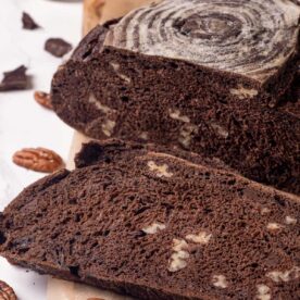 Square-framed sliced chocolate sourdough bread reveals the pecan and chocolate pockets defining its chewy open interior.